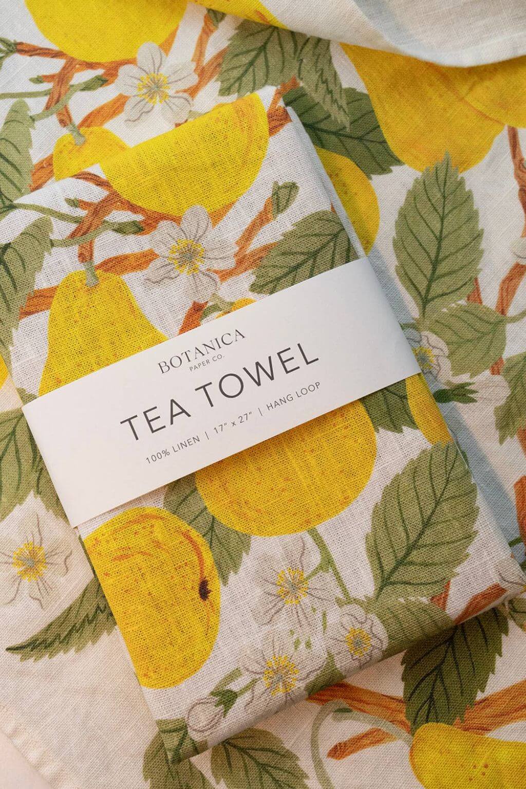 Folded Pear Orchard Linen Tea Towel on countertop, featuring golden pears and green leaves.