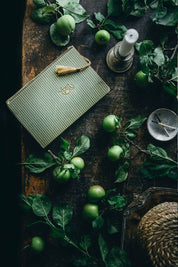 Green notebook with a tassel on a wooden surface with green apples and leaves.