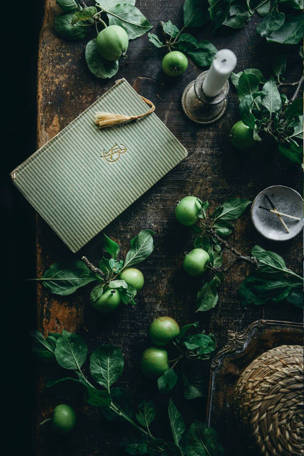 Green notebook with a tassel on a wooden surface with green apples and leaves.