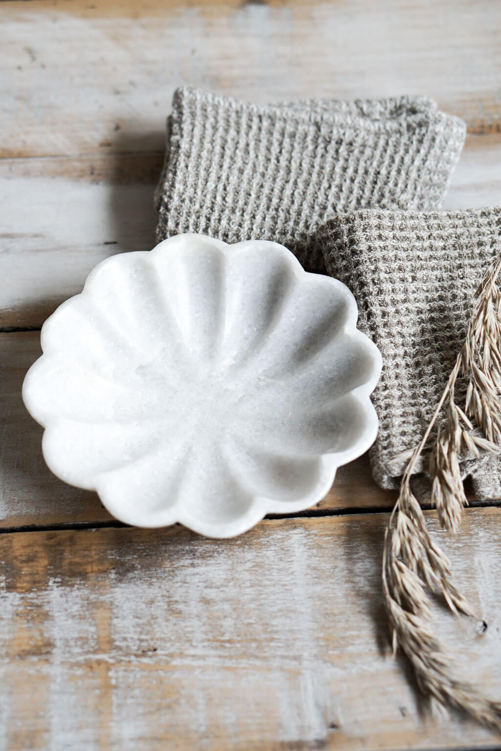 White marble fluted dish beside linen cloth and dried grasses