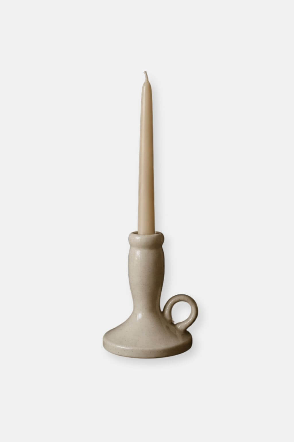 A single beige taper candle in a matching ceramic candlestick holder with a loop handle on the base, shown against a light gray background.