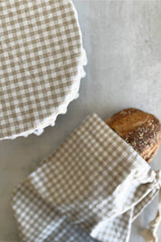 gingham linen bread bag holding rustic loaf with reusable bowl cover