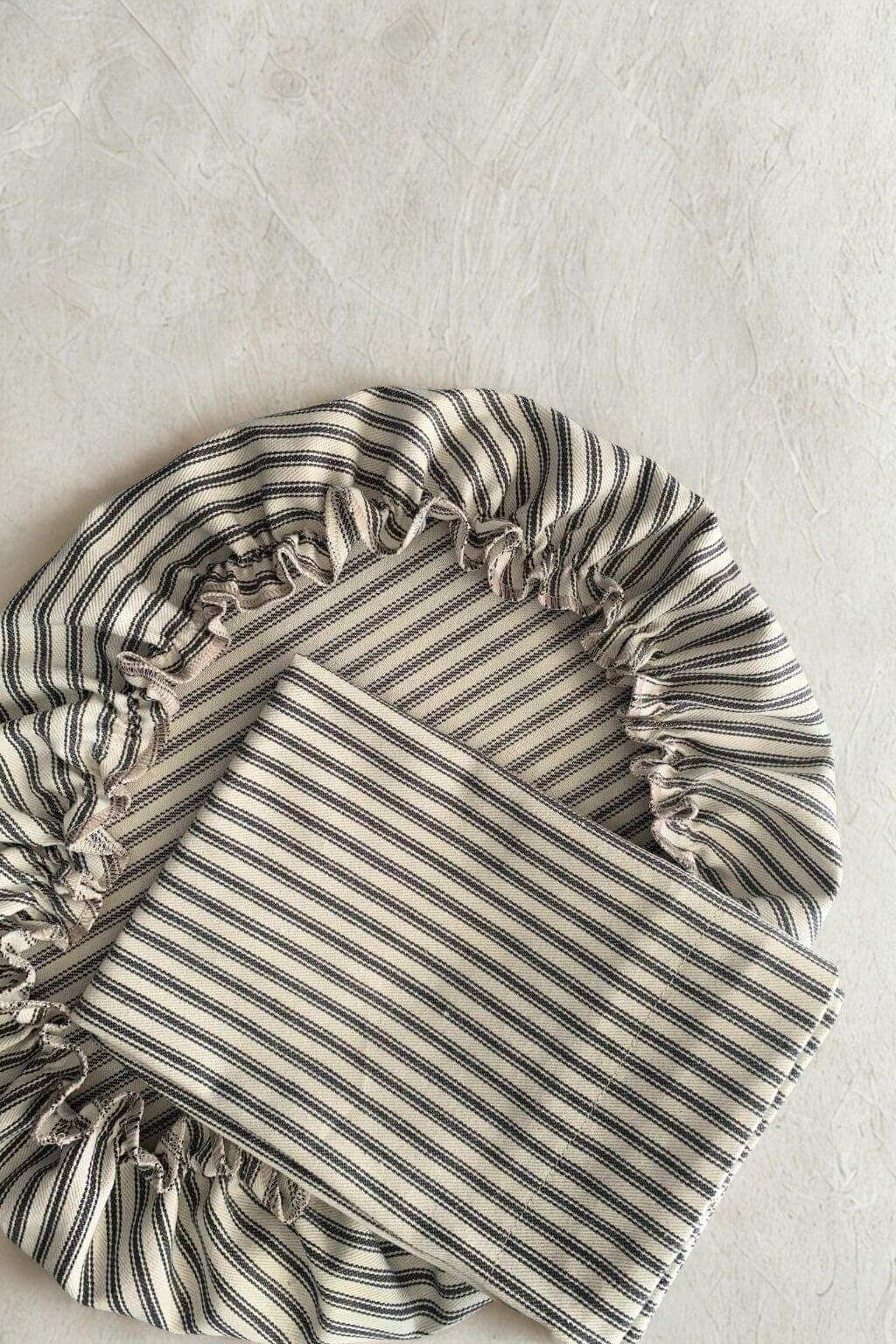 Ticking striped fabric bread bag and dough bowl cover on a light gray background