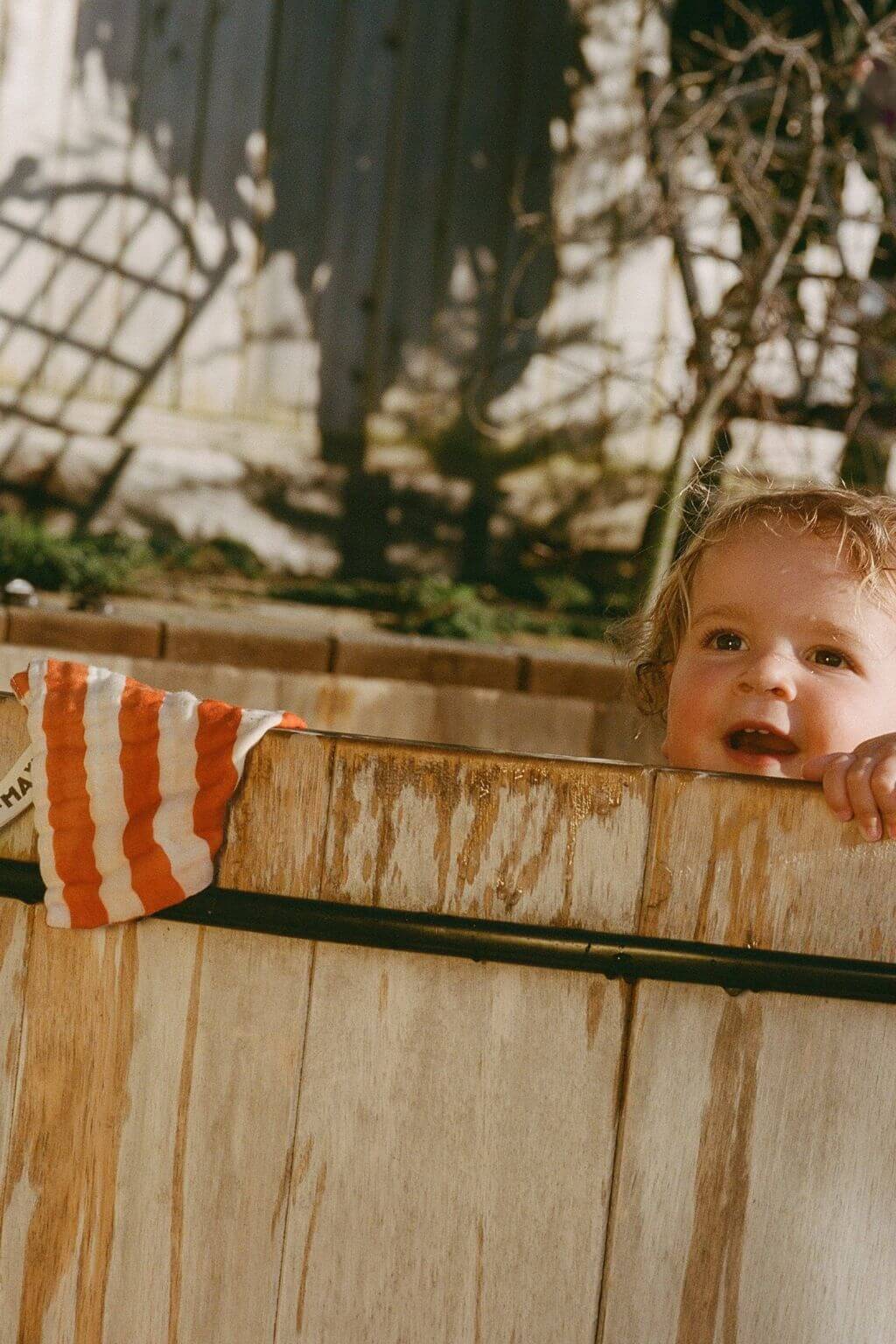 baby peeking over wooden tub with orange striped organic cotton washcloth