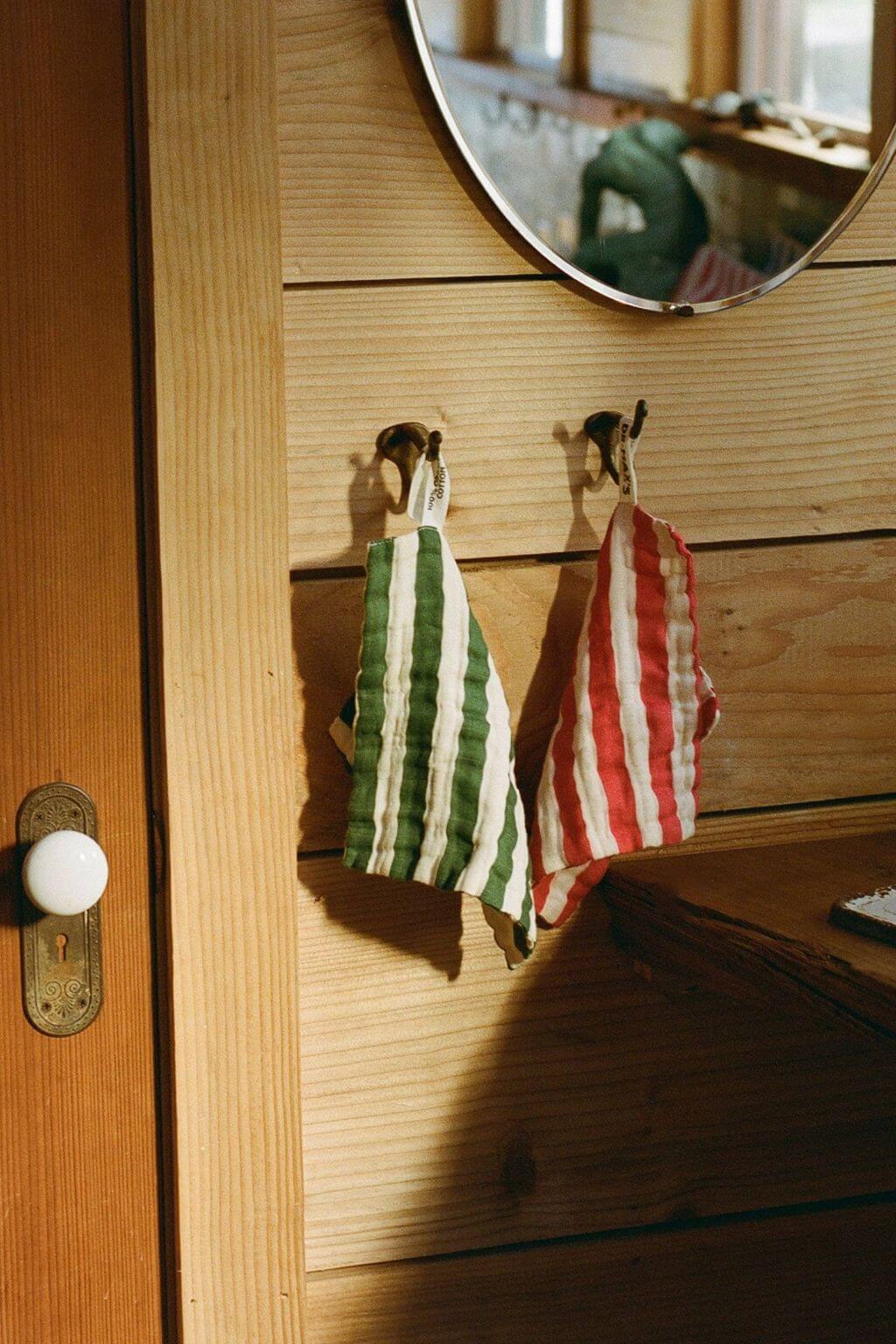 green and red striped organic cotton washcloths hanging on wooden wall hooks