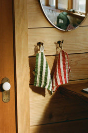 green and red striped organic cotton washcloths hanging on wooden wall hooks