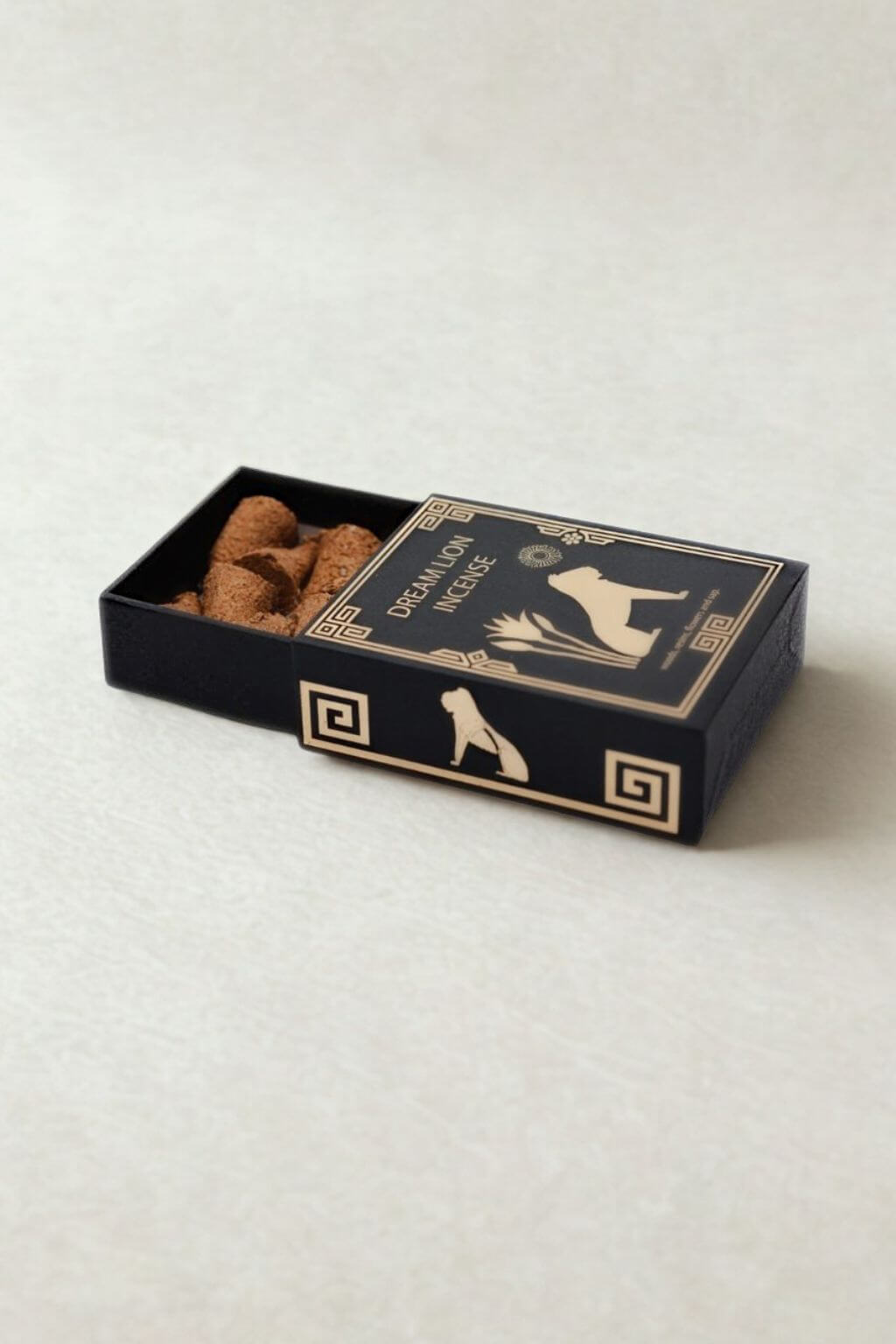 A black matchbox-style container with gold decorative graphics and the words 'Dream Lion Incense' on the lid, shown open with incense cones inside, photographed on a light neutral background.