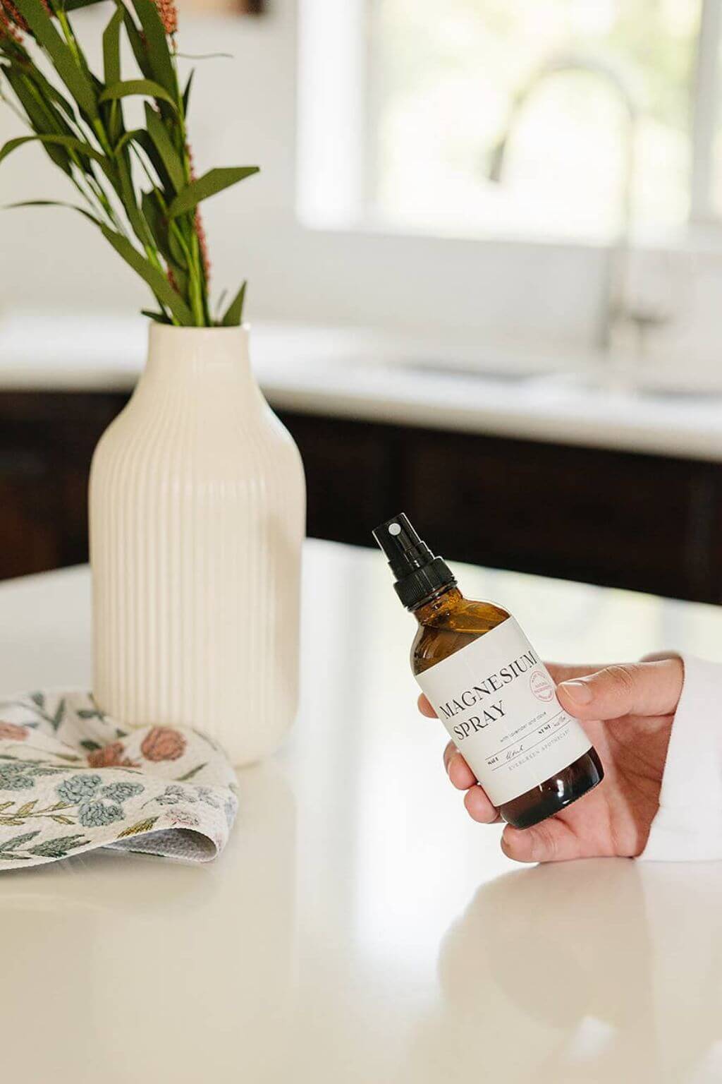 hand holding evergreen apothecary magnesium spray in bright kitchen setting
