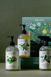 A set of Koala Eco Natural Cleaning Products, including hand wash, dish soap, and multi-purpose cleaner, displayed in front of a dark green gift box with botanical drawings.