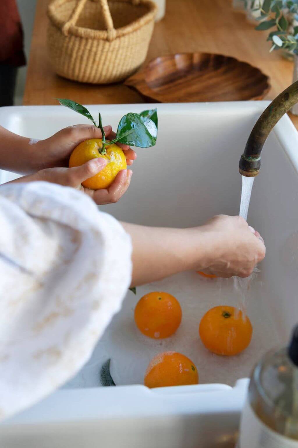 A woman washing fresh citrus fruit in a big farmhouse sink