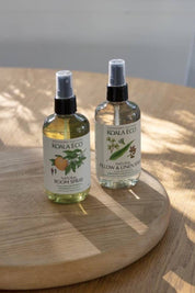 Two bottles of Koala Eco products on a wooden surface with sunlight casting shadows.