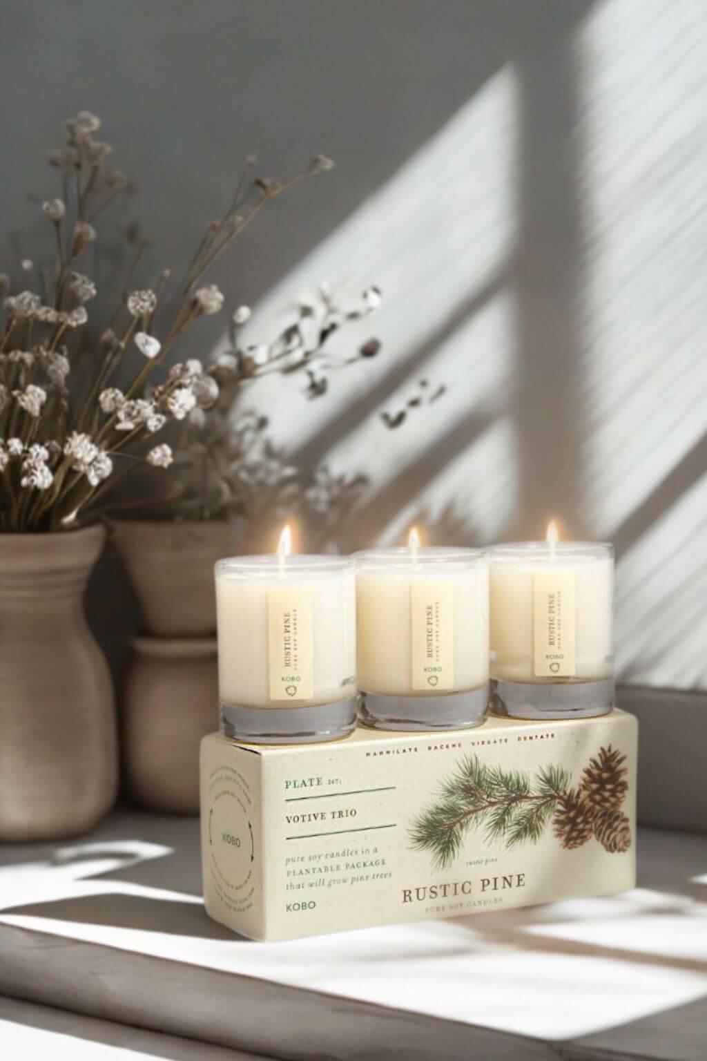 Three votive candles on a decorative box with a vase of flowers in the background