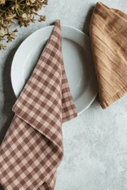 Chocolate gingham linen kitchen towel folded beside ceramic dinnerware