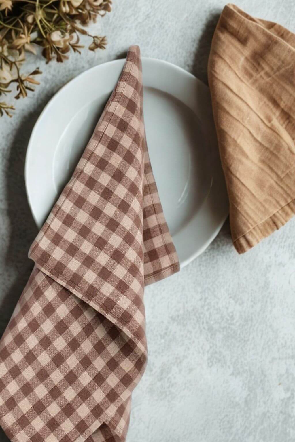 Chocolate gingham linen kitchen towel folded beside ceramic dinnerware