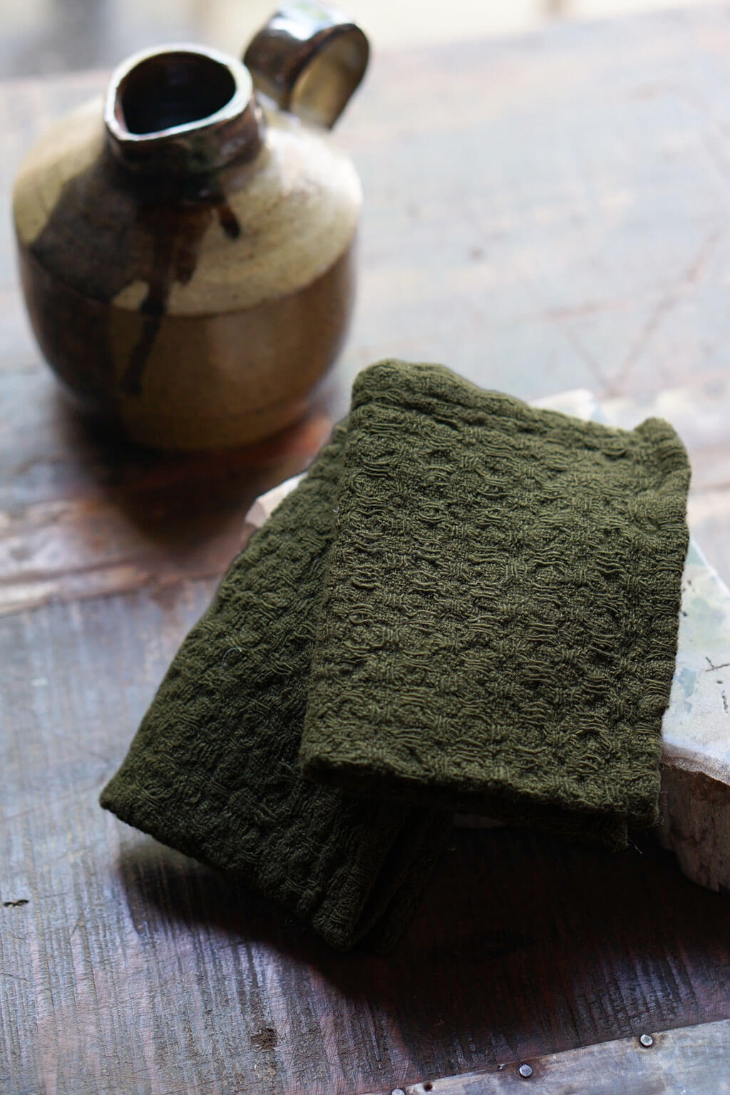 Martini olive waffle linen dishcloths styled beside rustic pottery vessel