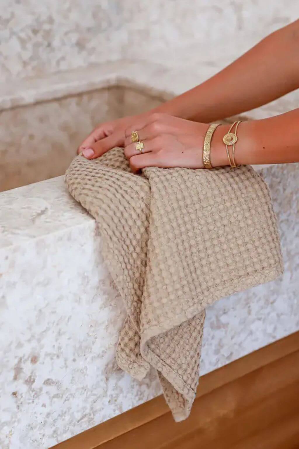 Person holding a beige textured kitchen towel on a marble sink