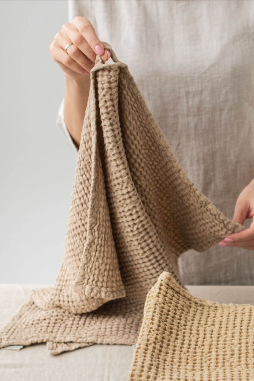Person holding a beige knitted towel against a neutral background