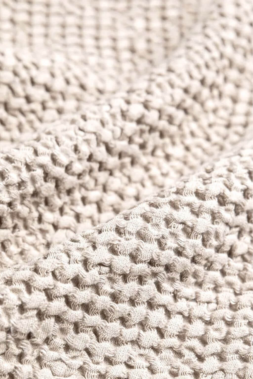 Close-up of a textured knit waffle fabric in a warm sand tone, showing the detailed looped stitch pattern and soft folds.