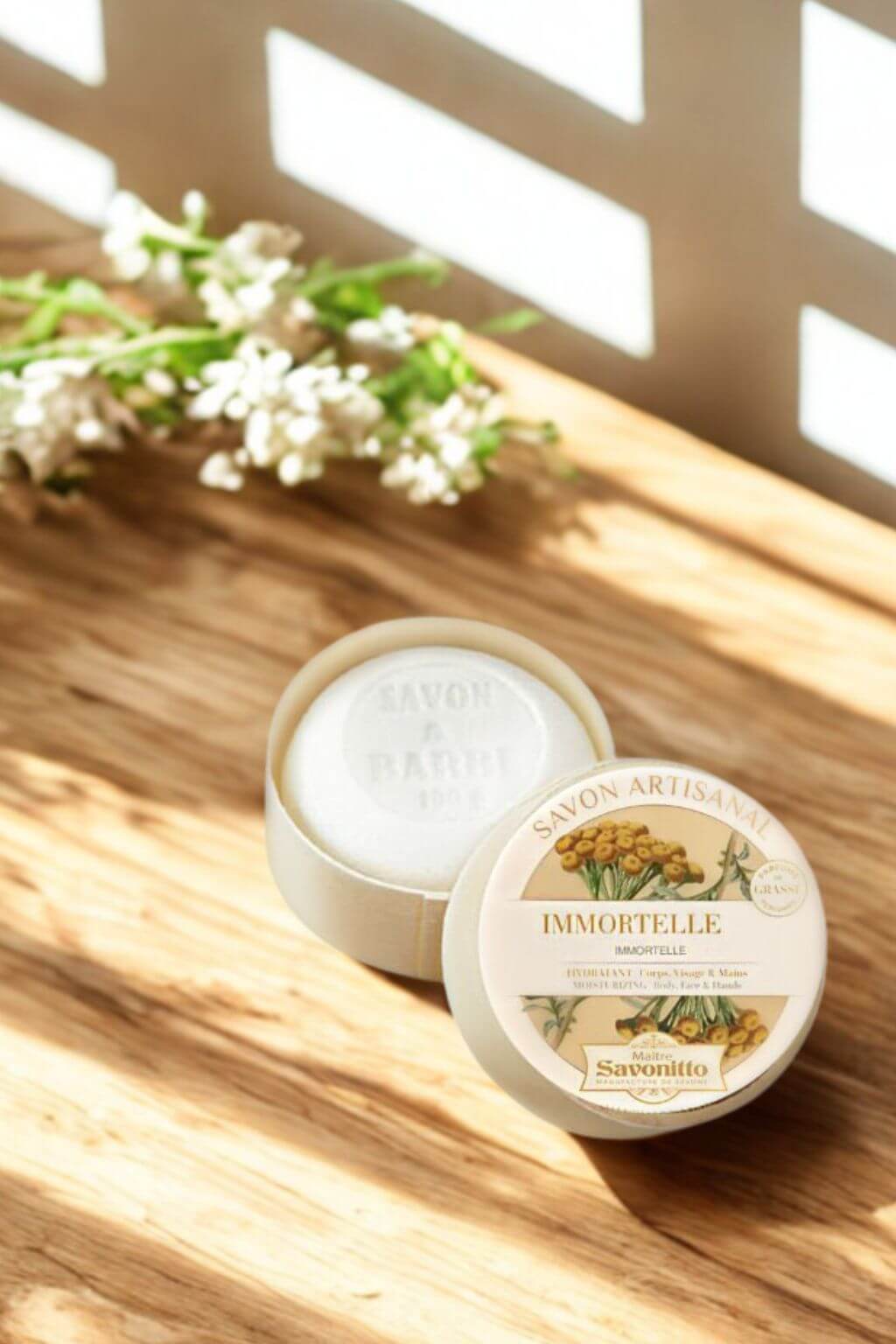 Wooden container with Savo Immortelle soap on a wooden surface with flowers.
