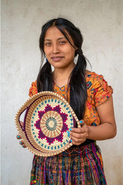 Woman holding a colorful woven basket against a plain background