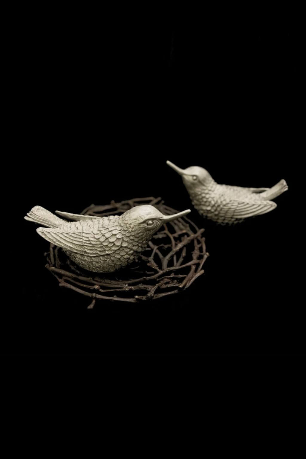 Two small humingbird salt and pepper shakers in a textured antique pewter finish, perched on a twig nest against a solid black background.