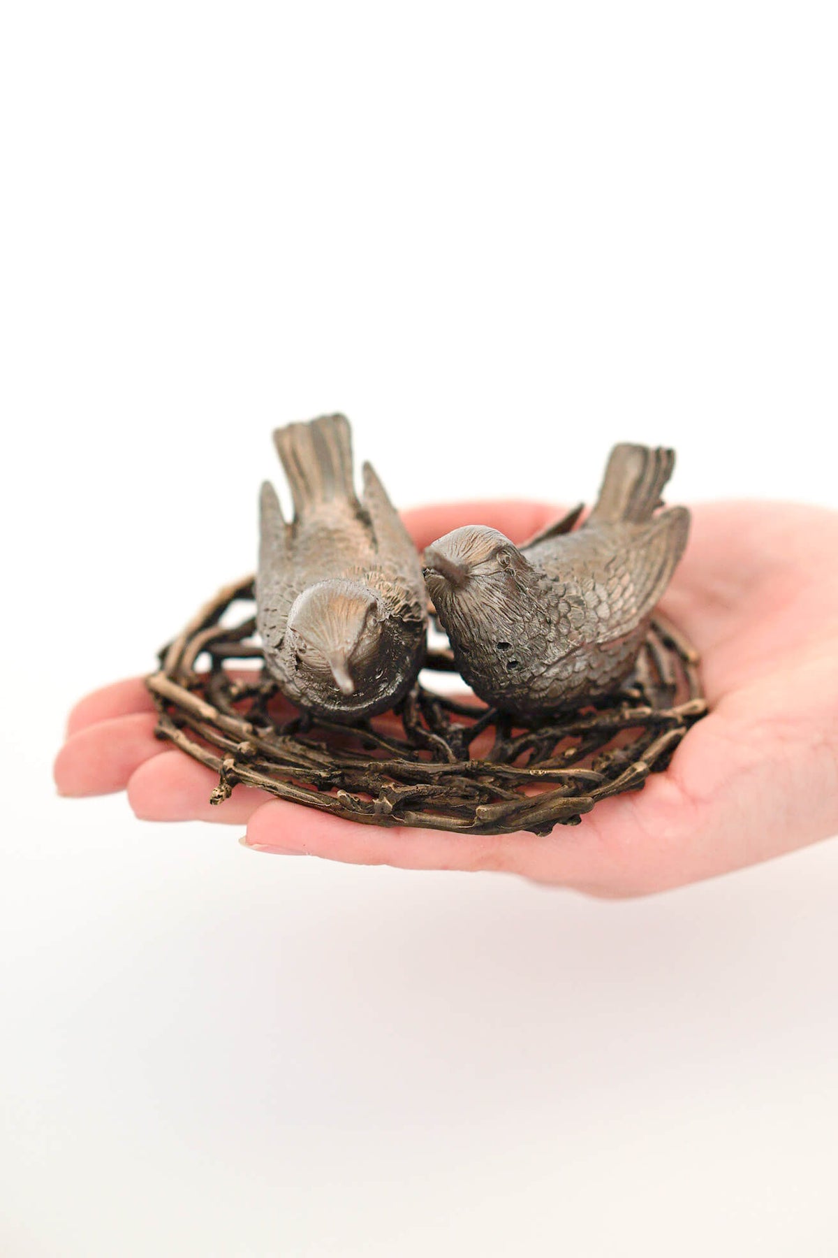 Small hummingbird salt and pepper shakers resting in hand on twig nest tray