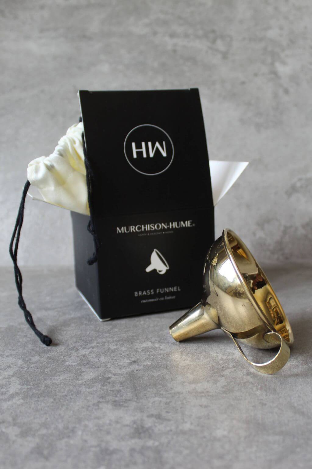 Gold brass funnel with Murchison-Hume packaging on a gray surface