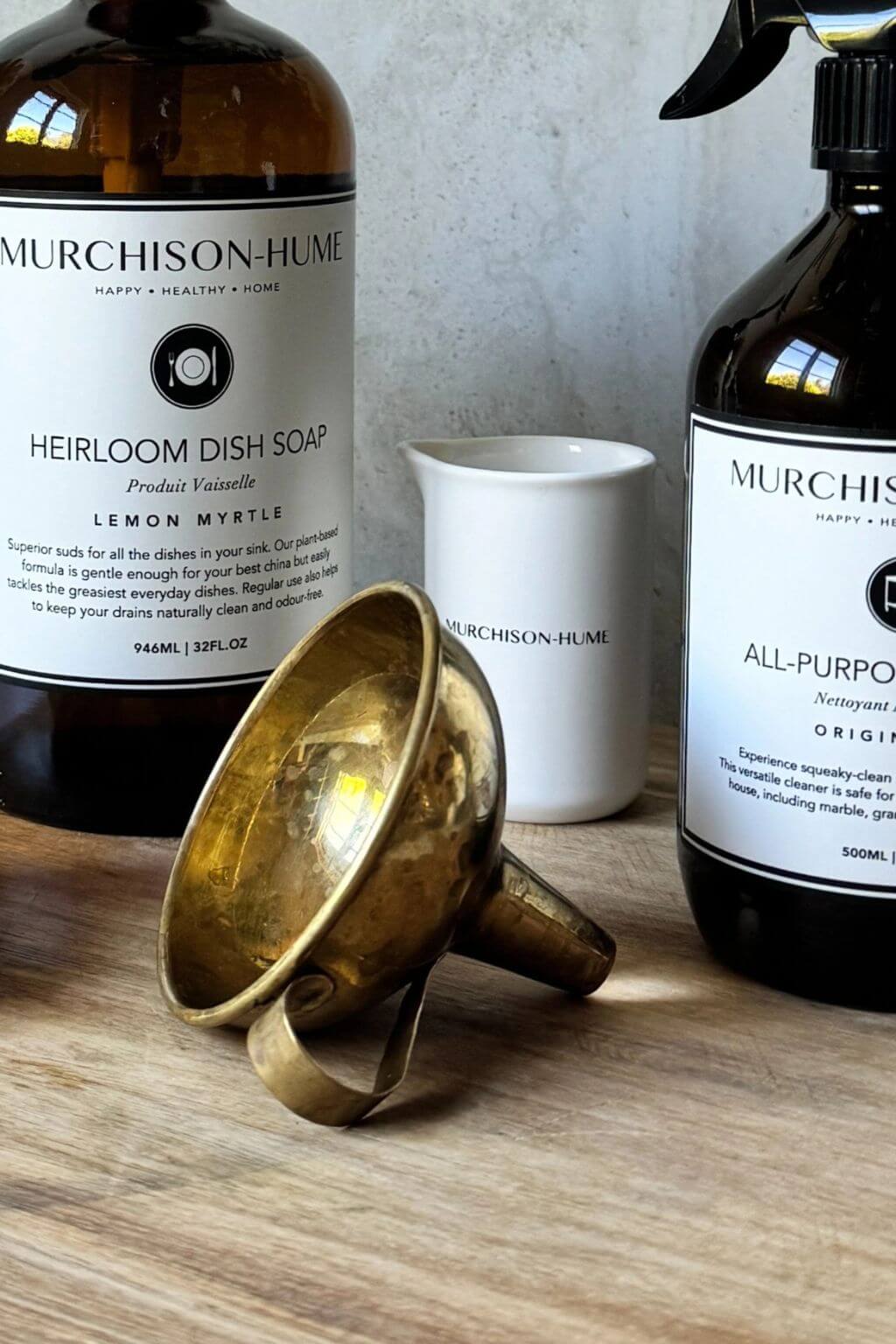 Two Murchison-Hume bottles and a brass funnel on a wooden surface.