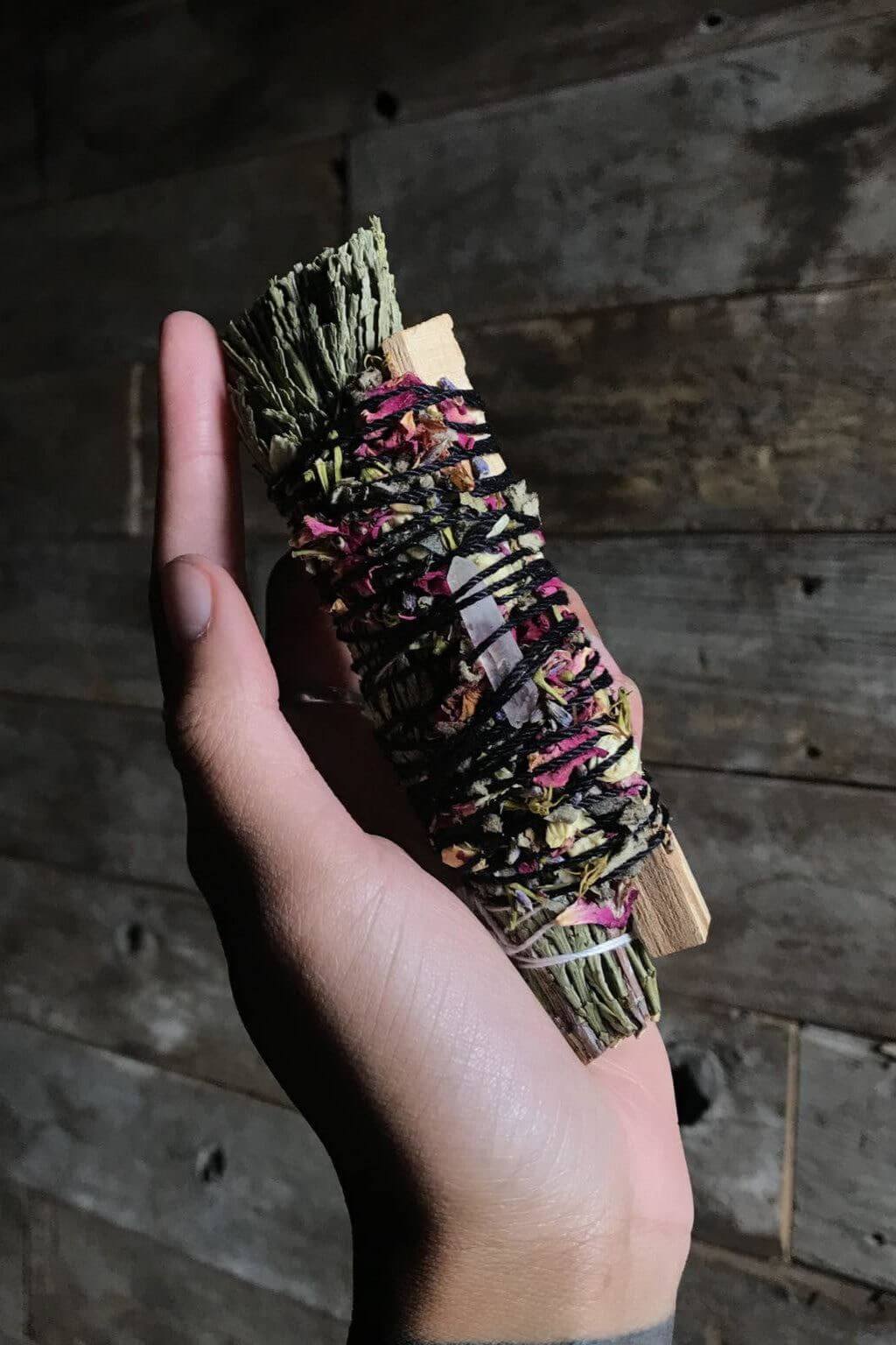 hand holding smudge bundle with palo santo and cedar