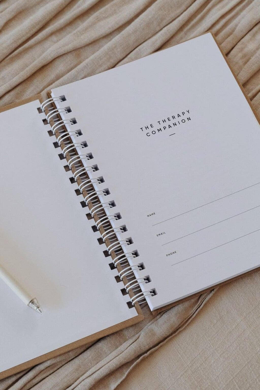 Open spiral-bound notebook titled 'The Therapy Companion' on a beige fabric background