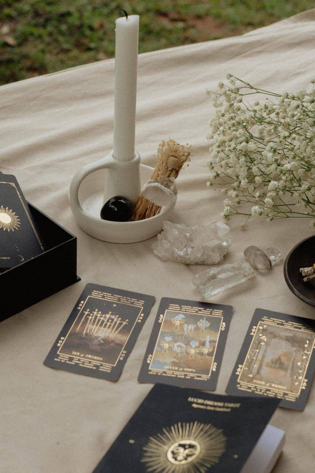 Cloth draped outside on the grass with Lucid Dream Tarot Spread, guidebook, taper candle, crystals and baby's breath