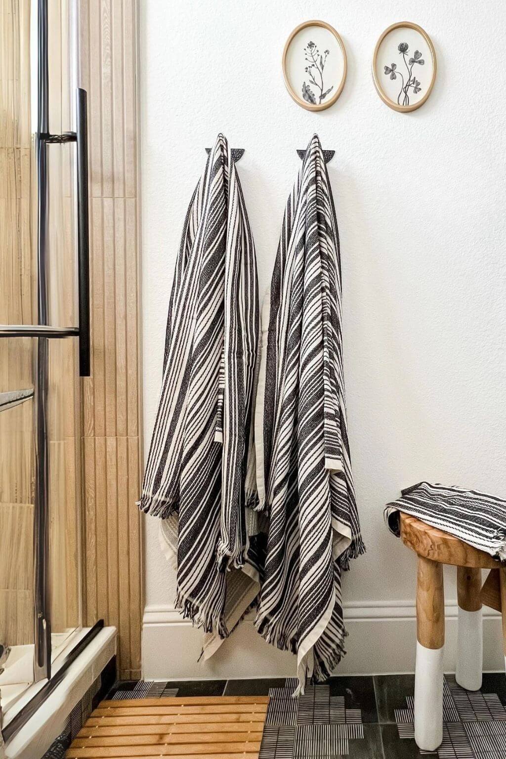 Striped towels hanging on a rack in a bathroom with wooden stool and framed botanical pictures.