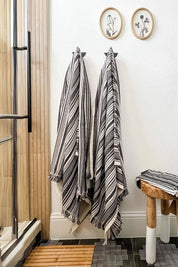Striped towels hanging on a rack in a bathroom with wooden stool and framed botanical pictures.
