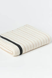 Folded towel with black and terracotta stripes on a cream background