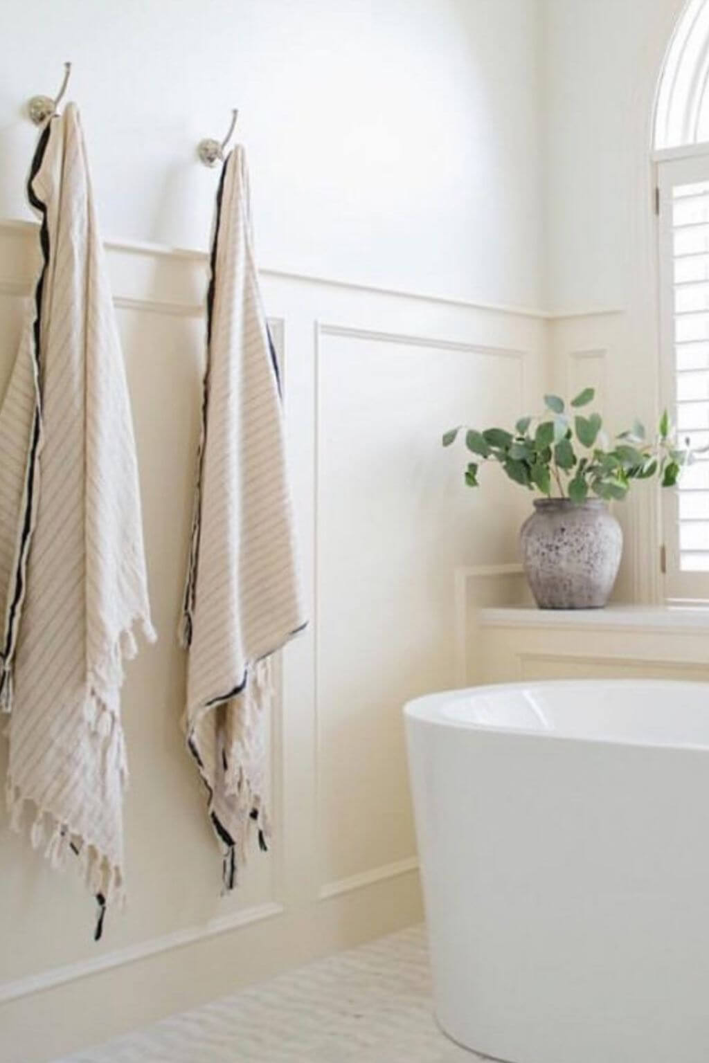 Bathroom with white freestanding bathtub, towels hanging on a rack, and a plant on a windowsill.