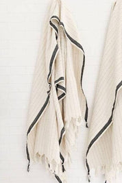 Beige Turkish towel with black stripes and fringes on a white background