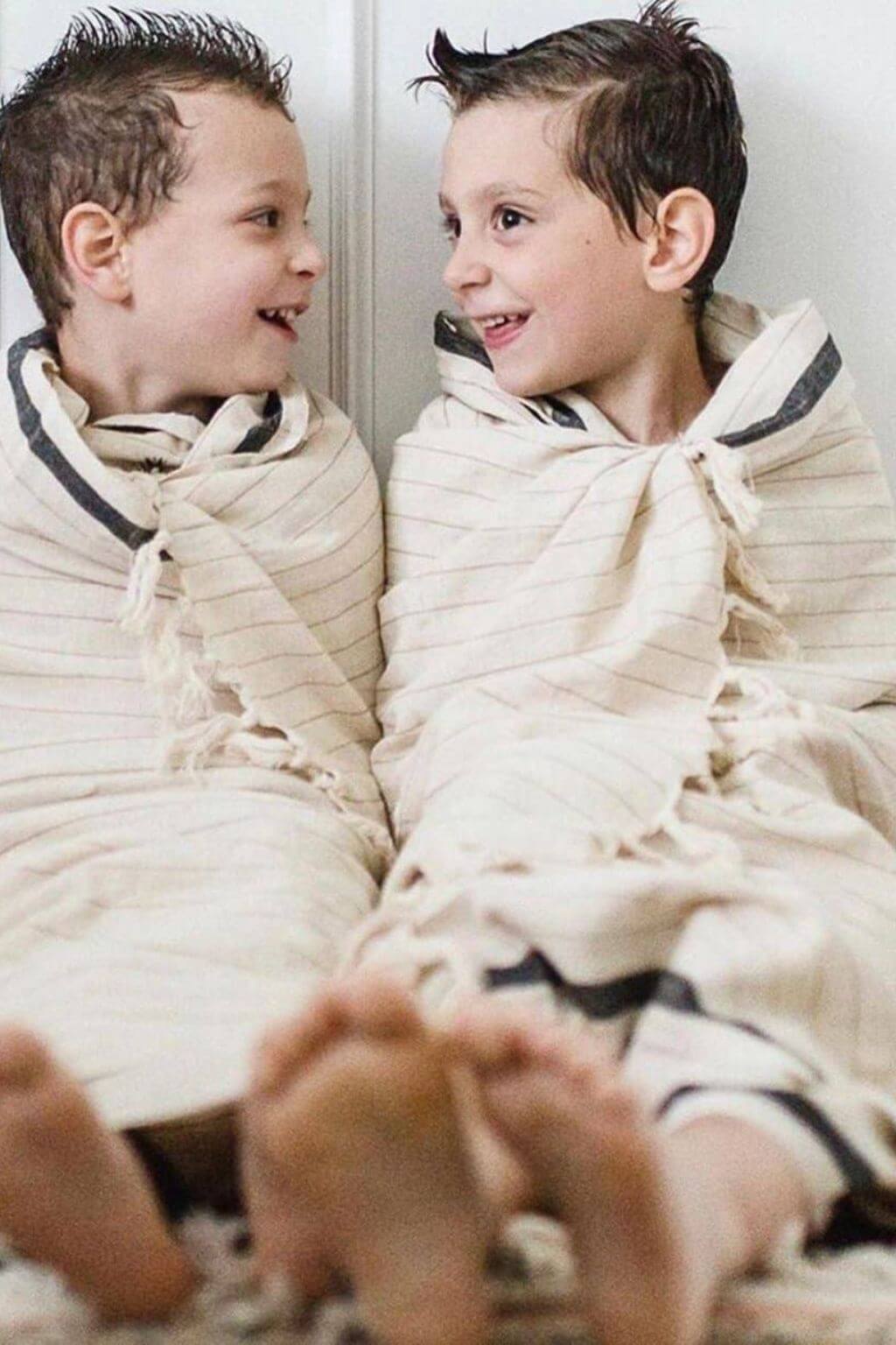 Two children wrapped in a blanket sitting close to each other.