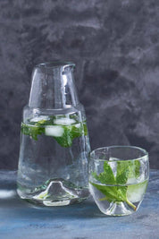 A pebbled glass carafe filled with water and ice cubes, alongside a matching glass, both placed on a blue surface.
