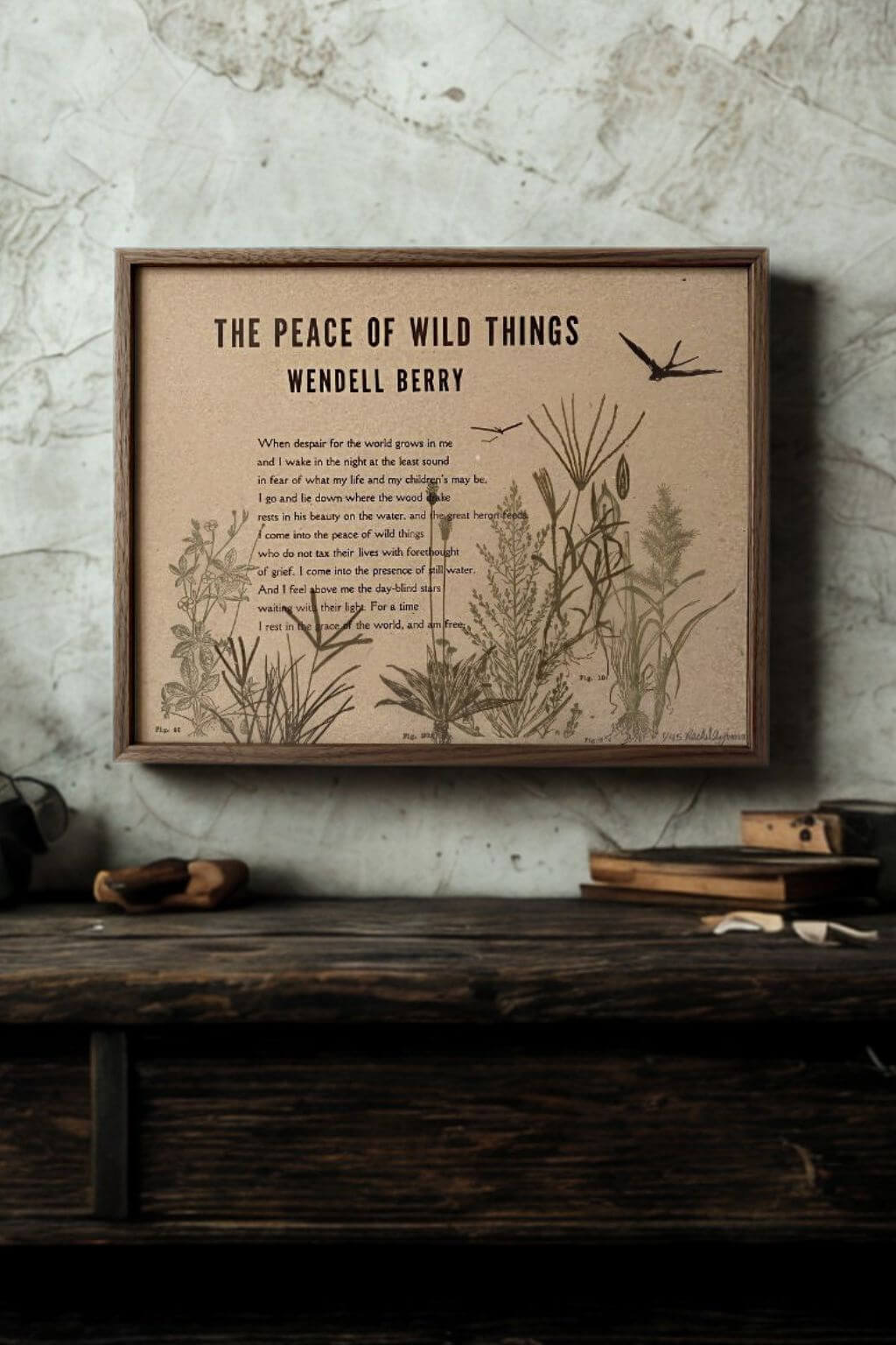 A framed art print featuring Wendell Berry's poem 'The Peace of Wild Things' with botanical illustrations, displayed on a rustic wooden shelf against a textured gray wall.
