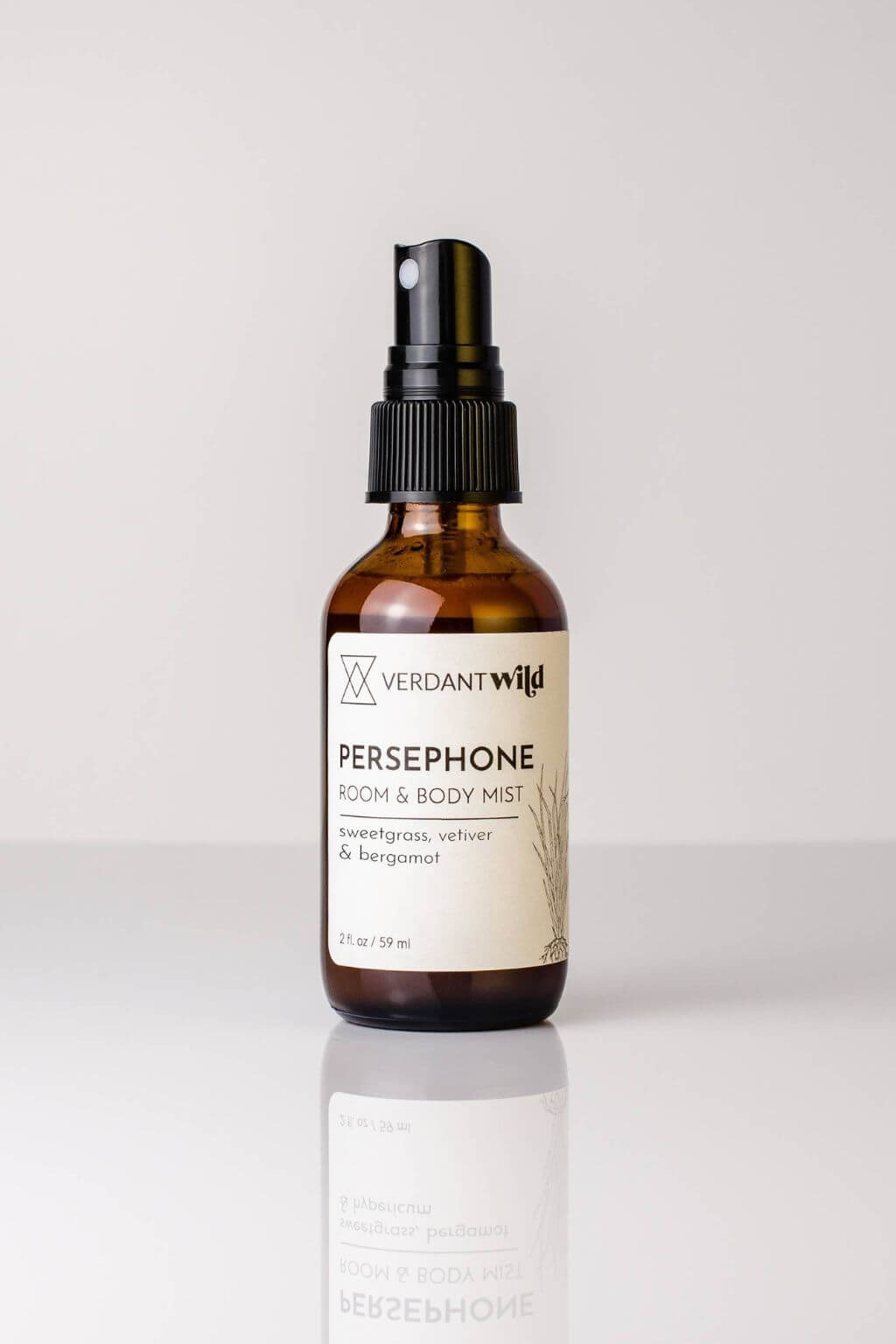 Amber Glass Spray bBottle of Persephone Room + Body Mist on a white background with a reflective surface
