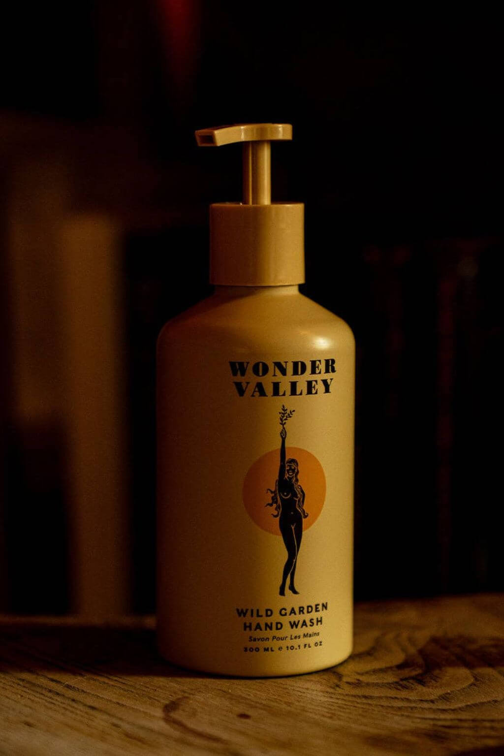 Wonder Valley Wild Garden Hand Wash in a beige pump bottle with a wooden-style dispenser, set on a rustic wooden surface against a dark, warm-toned background.