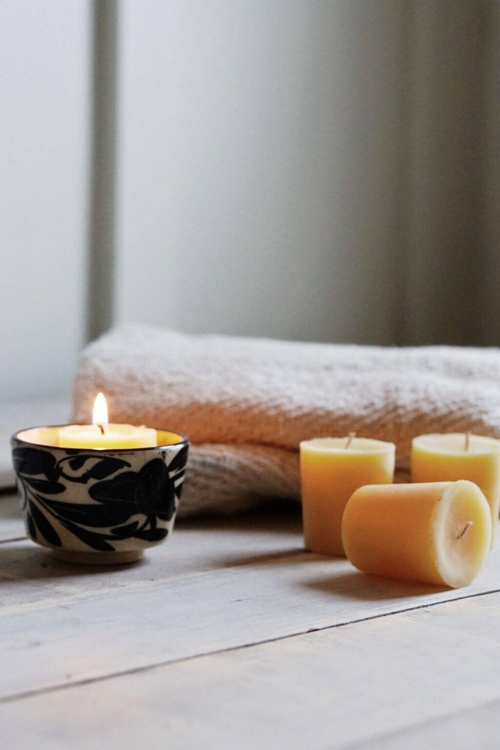 Beeswax Votive Candle in a vintage black and white cup with three beeswax votive candles on a wooden surface.