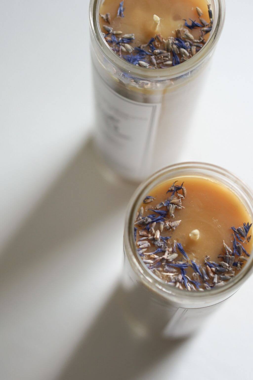 Two glass candles with dried lavender flowers on a white surface