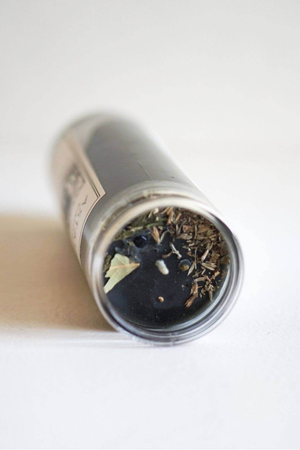 A close up of a cylindrical candle lying on its side, showing dried botanical material and black beeswax