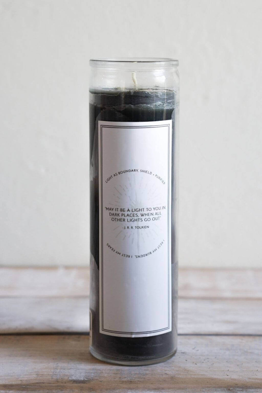 A tall black candle in a clear glass jar with a white rectangular label with a white background