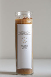 A tall glass jar candle with a white label, filled with light brown beeswax and topped with a small amount of brown and tan herbs. The label reads 'BEARER OF FRUIT' and 'SOUL PURPOSE CONFIDENCE WITNESS RADIANCE'.
