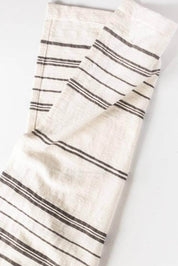 A folded off-white linen kitchen towel with thin dark gray horizontal stripes, shown on a plain white background.