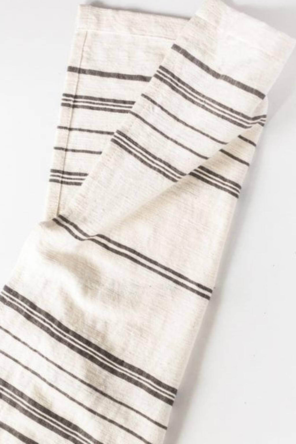 A folded off-white linen kitchen towel with thin dark gray horizontal stripes, shown on a plain white background.