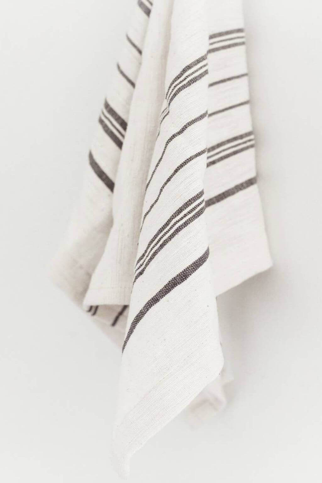 White towel with charcoal stripes hanging on a white background