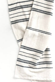 A close-up of a folded white tea towel with thin navy stripes